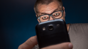 Homem de óculos observando uma blocklist em seu celular.