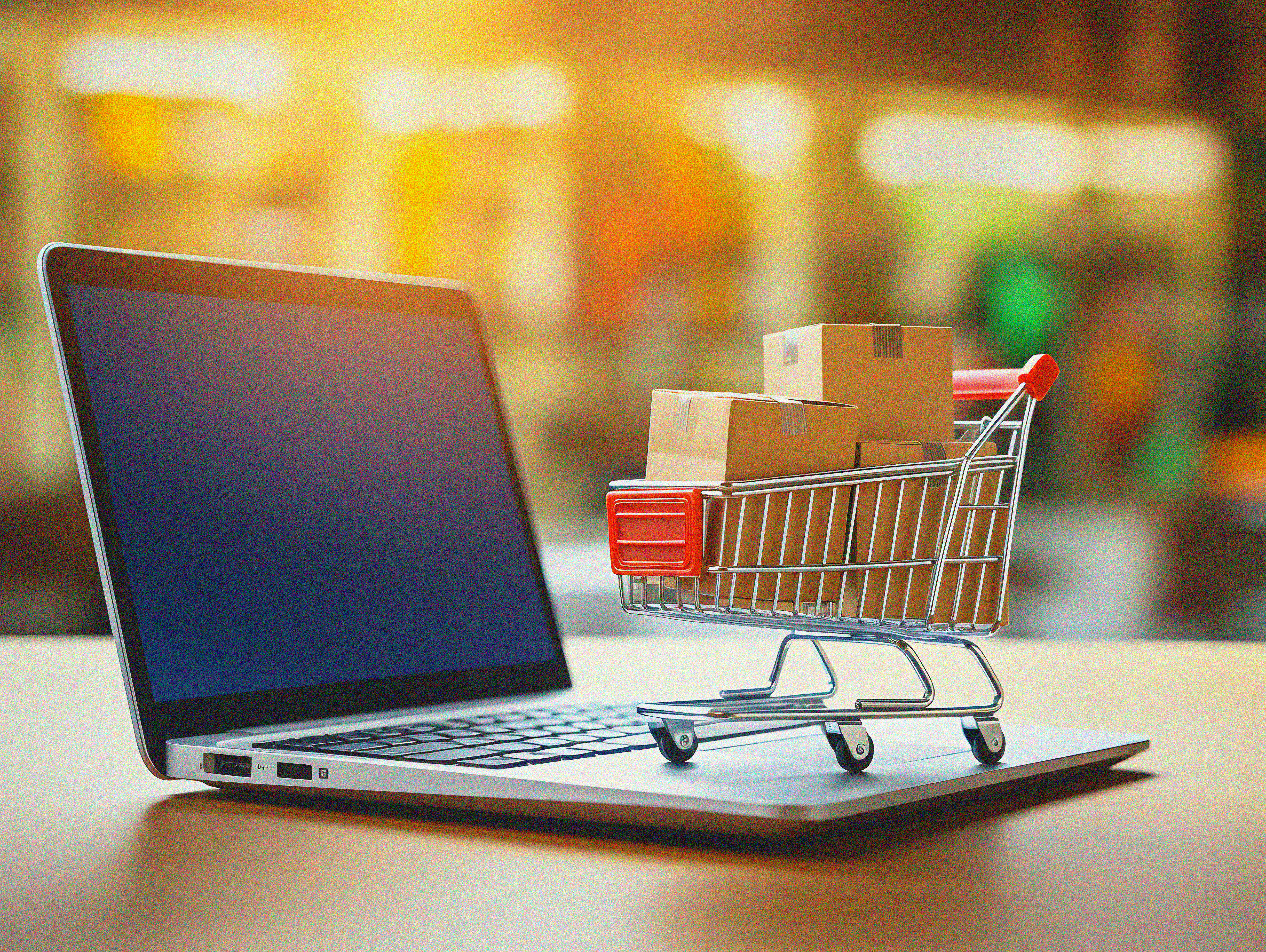 Computador acessando e-commerce com um pequeno carrinho de compras sobre o teclado.